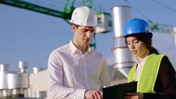 La giovane donna ingegnere e l'uomo d'affari hanno una discussione sulla parte superiore del cantiere che utilizzano un tablet digitale per analizzare qualche piano di costruzione indossano caschi di sicurezza — Video Stock