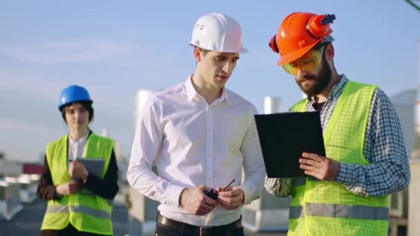 Discussing on the construction site between diverse specialists lady take a digital tablet to showing the plan of construction they wearing safety helmets. 4k — Stock Video