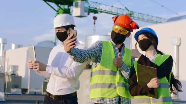 Op de pandemie met coronavirus groep van ingenieurs en architect met beschermend masker op de top van de bouwplaats neem een aantal foto 's met behulp van de smartphone ze dragen veiligheidshelmen — Stockvideo