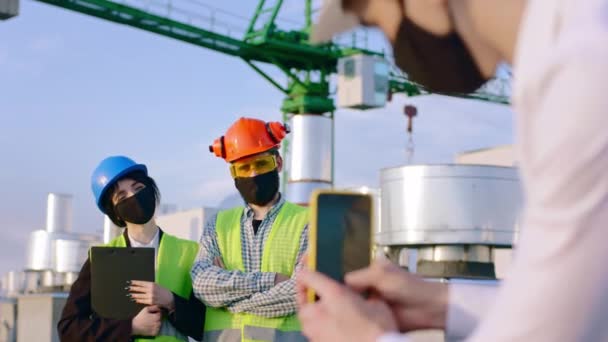 Alla fine della giornata in un cantiere due giovani ingegneri in posa davanti allo smartphone scattano alcune foto indossando una maschera protettiva sulla pandemia di COVID-19 e attrezzature di sicurezza — Video Stock