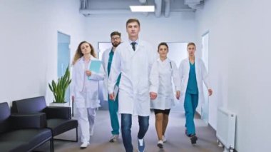 Kameranın önünde modern hastane koridorunda büyük bir grup doktor ve hemşire kameranın önünde durup poz veriyorlar.