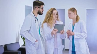 Karizmatik olgun doktor bayan ve hastane koridorunda dijital tabletteki hastanın teşhisini analiz eden iki hemşire.