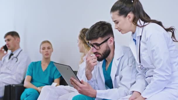 Atractivo grupo de estudiantes de medicina y su médico tienen un pequeño descanso el médico hombre hablando por teléfono y otros estudiantes toman la tableta digital para discutir alguna enfermedad — Vídeos de Stock