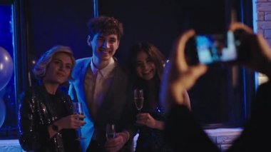 Balo gecesi partisinde genç ve karizmatik öğrenciler komik poz verirken diğer genç öğrenciler de akıllı telefondan fotoğraf çekiyorlar. ARRI Alexa Mini 'de çekilen