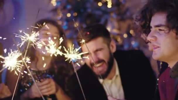 Большая группа молодых друзей с улыбкой, празднующих новый год вместе, они взволнованы, держа несколько блесток в руке и наслаждаясь временем вместе — стоковое видео