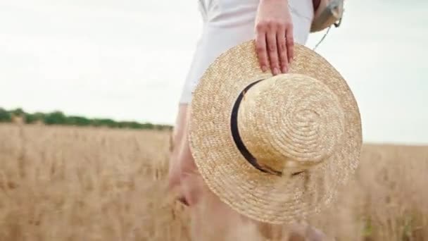 Par une journée ensoleillée au milieu d'un grand champ de blé marchant femme dans un short blanc à travers le champ, elle tenant un chapeau de pays à la main — Video