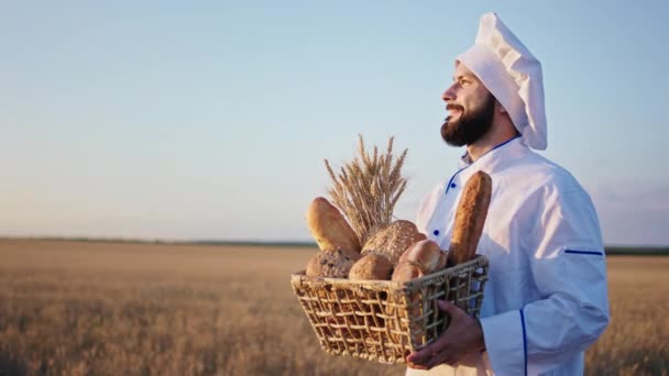 Al tramonto in mezzo al campo di grano panettiere uomo in possesso di un grande cesto di un pane fresco e sorridente grande — Video Stock