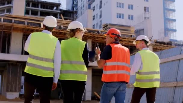 Uprostřed staveniště předák a další inženýři a architekt analyzující plán staveniště mají vážnou diskusi — Stock video