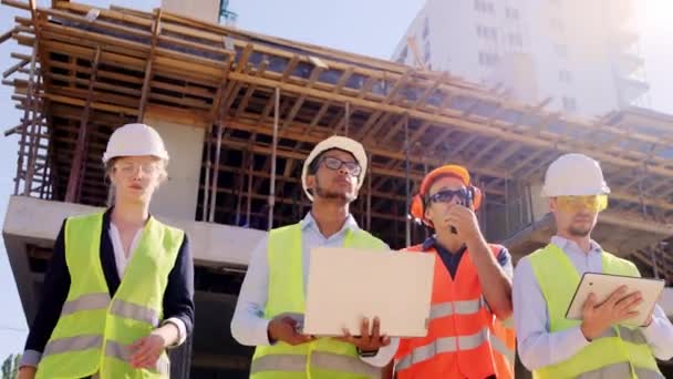 Multiethnic group of diverse specialists and middle -aged foreman walking down the construction site using digital tablet and laptop to analyzing the next step in construction mature man using ration — Stock Video