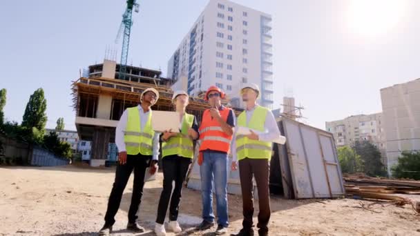 Moderne bouwplaats voorman van middelbare leeftijd met behulp van een rantsoen te hebben een bespreking met andere specialisten vormen de top van de site, terwijl andere specialisten zijn het analyseren van het plan van het gebouw — Stockvideo