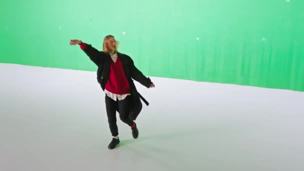 Перед камерой молодая женщина танцует и наслаждается временем с собой в зеленом фоновом студии — стоковое видео