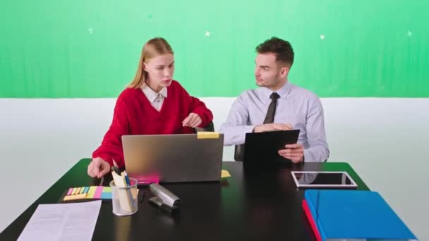 漂亮的金发女士坐在工作台上与办公室经理讨论，他们用笔记本电脑和数码平板电脑在一个彩色钥匙工作室里制定了一些策略 — 图库视频影像