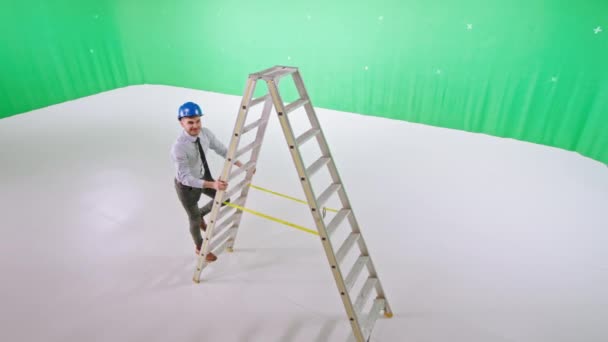 Chroma κλειδί στούντιο όμορφος αρχιτέκτονας τύπος με κράνος ασφαλείας ποζάρουν μπροστά από την κάμερα, ενώ στέκεται σε μια σκάλα — Αρχείο Βίντεο