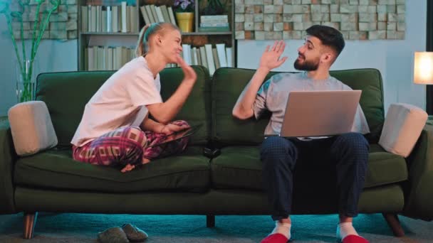 ソファに座っているリビングルームの幸せなカップルは一緒に彼らがこれのためにラップトップと電子タブレットを使用してインターネット上で何かを見つけようとする楽しい時間を持っています。ARRIアレクサミニで撮影 — ストック動画