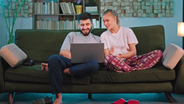 In een moderne woonkamer op de bank paar hebben een discussie samen ze terwijl kijken naar iets op de laptop ze glimlachen samen groot — Stockvideo