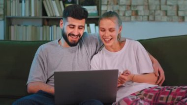 Gülümseyen büyük çift kanepede otururken sohbet ederken bir dizüstü bilgisayar kullanıyorlar.