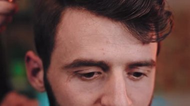 Çekici bir adamın kamera önünde saç tıraşı olmak için profesyonel kırpıcı kullanan bir berber var. 4k