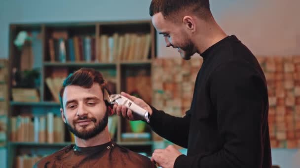 Zu Hause gut aussehende Kerl haben einen professionellen Friseur mit professionellen schwarzen Clipper, um die Haare zu schneiden — Stockvideo