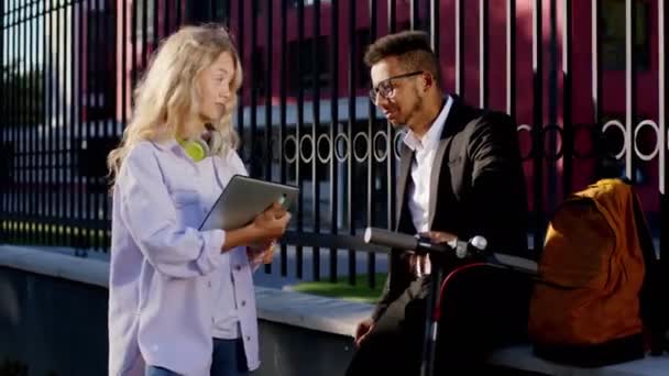 Conversa amigável entre dois estudantes senhora e cara eles discutindo algo interessante após a faculdade fazer uma parada no meio da rua loira mulher cabelo segurando digital tablet cara — Vídeo de Stock