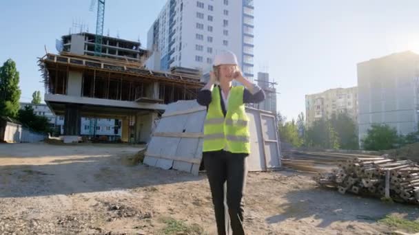 Sur le grand chantier de construction jeune femme ingénieur commencer à danser tout en tenant les écouteurs à l'heure du déjeuner, elle est venue à toute l'équipe ils dansent ensemble portant du matériel de sécurité — Video