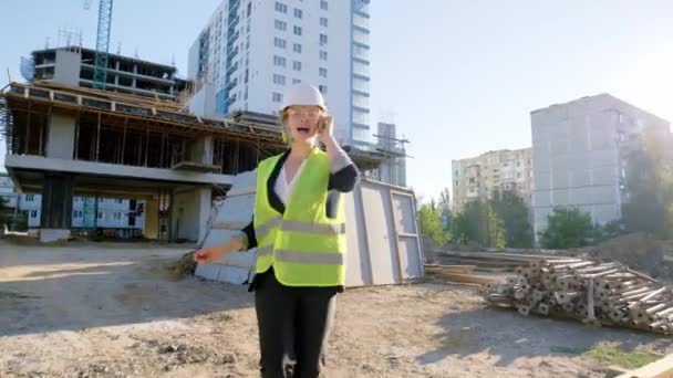 Boldog és izgatott mérnök hölgy a szünetben zenét hallgatni a fejhallgatóból, és elkezdeni táncolni az építőmunkásokkal együtt biztonsági felszerelést viselnek. — Stock videók