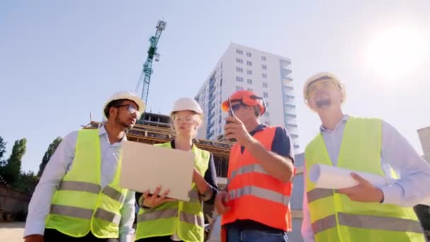 Multiethnische Gruppe von Ingenieuren und Architekten Analyse des Arbeitsplans mit dem Polier mit Laptop und digitalem Tablet nimmt er die Ration zu inerten Spezialisten den nächsten Schritt zu erklären, um sie zu arbeiten — Stockvideo