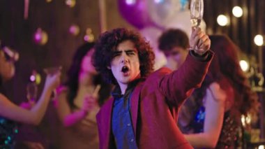 Kameranın önündeki heyecanlı genç adam büyük, büyüleyici bir partide atmosferin tadını çıkarıyor. Bir bardak şampanya tutuyor ve anın tadını çıkarıyor.