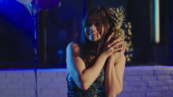 A diákbulin karizmatikus, gyönyörű, fiatal nő viccelődik egy ananásszal, aki élvezi az estét a kamera előtt. — Stock videók