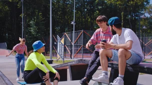 Tempo di relax per un gruppo di amici adolescenti bello cercando nel bel mezzo del moderno skate park signora capelli biondi è venuto su uno skateboard per i suoi amici che socializzare e trascorrere grande tempo — Video Stock