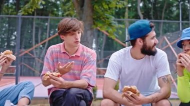 Aç bir grup genç öğle yemeği için kaykay parkına gidip kameranın önünde hamburger yiyor. ARRI Alexa Mini 'de çekilen