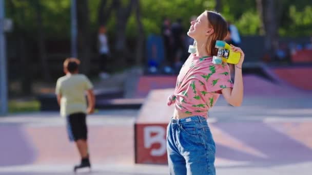 У сонячний день молода жінка насолоджується часом у сучасному скейт-парку, який вона стоїть перед камерою усміхнений великий взяти її скейтборд, щоб почати їзду — стокове відео