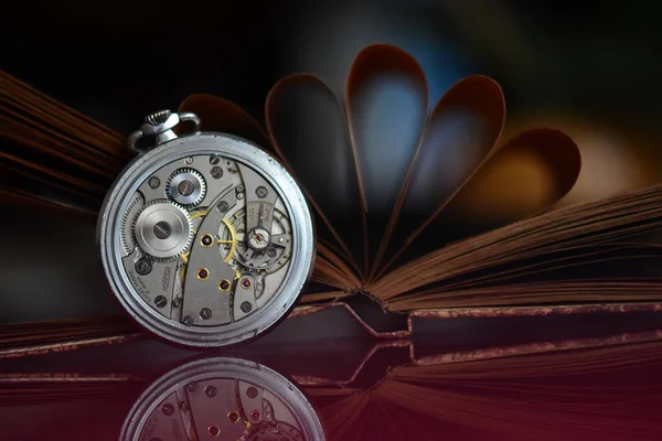 Old pocket watch and book on a mirror surface