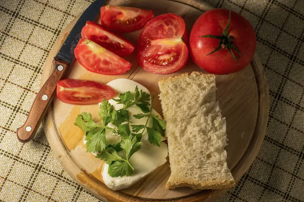 Night snack, tomatoes, herbs, bread and cheese on a wooden board on the table.