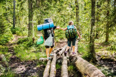 Genç adam ağaçlar köprüsünü geçerken kızı elinden destekler. İki kişi ormanda yürüyüşe çıkıyor.