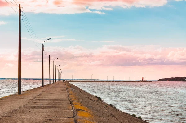 Sea road to the pier. Embankment with lanterns in the evening against the background of the sunset sky