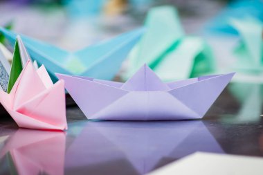 Birkaç kağıt tekne ayna yüzeyinde duruyor. Basit gemilerin yapımında usta origami sınıfı.