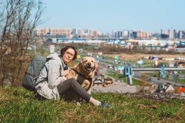 Şehrin arka planında bir dağda Labrador Retriever 'a sarılan bir kız. Şehirde bir köpekle tatil.