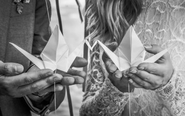 Kâğıt turnalar kadın ve erkeklerin avuçlarında öpüşürler. Düğünün dekorasyonu için Origami.