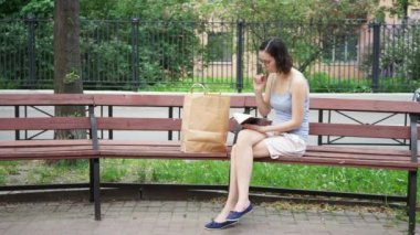 Bir kız bankta oturuyor ve bir kitabı karıştırıyor.