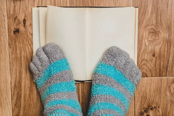 Striped socks with toes on the background of an open book on the wooden floor. Comfortable clothing for the legs at the weekend.