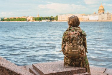 Saint Petersburg, Rusya-7 Temmuz 2020: Sırt çantalı bir kadın turist nehir kıyısında oturur ve şehre bakar. Büyük bir şehirde tek başına yürümek.