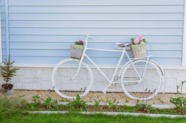 Evin yanında elinde çiçek sepeti olan eski beyaz bir bisiklet duruyor. Provence tarzında avlu dekoru.