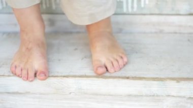 Bir verandanın boyalı ahşap basamaklarında duran bir bebeğin yalınayak ayakları.