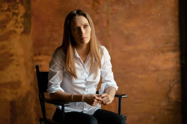 Genç güzel duygusal şehvetli kadın sandalyede oturan beyaz gömlekli portresi.