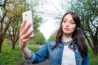 Yanında yeşil park smartphone selfie alarak genç gülümseyen kadın.