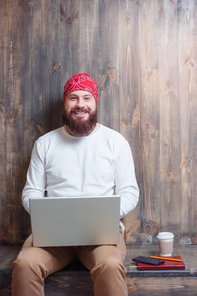 Young bearded man using laptop while sitting over wooden background.
