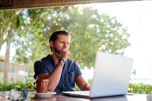 Young  bearded man using laptop while sitting on summer terrace.