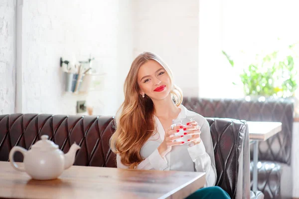 Young beautiful long hair woman holding cup of beverage while sitting at cafe.