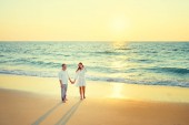 Fiatal, szerelmes pár, gyaloglás együtt a homokos tengerparton élvezi a tenger és a naplemente.