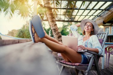 Tropik sahilde kafede dizüstü bilgisayar kullanan genç ve güzel kadın.